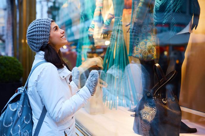 Jong meisje met blauwe jas, must en handschoenen kijkt naar kleding in etalage