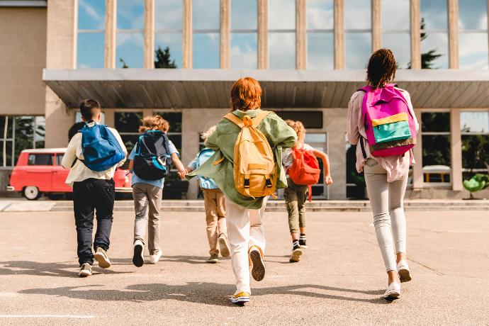 Groep kinderen met gekleurde rugzakken lopen naar school