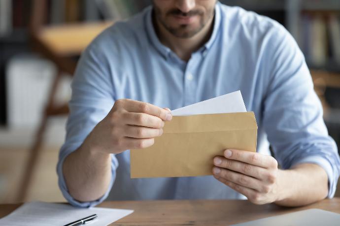 Man opent een bruine envelop met een witte brief erin